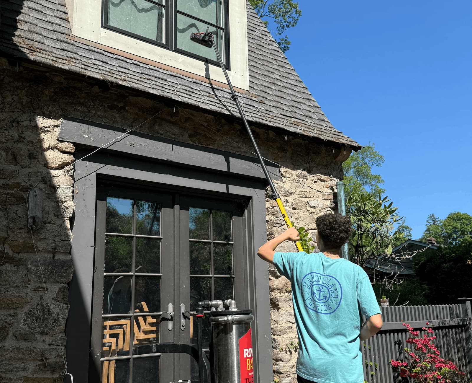 Window cleaning technician using a water-fed pole brush to clean upper windows on a Westport stone home